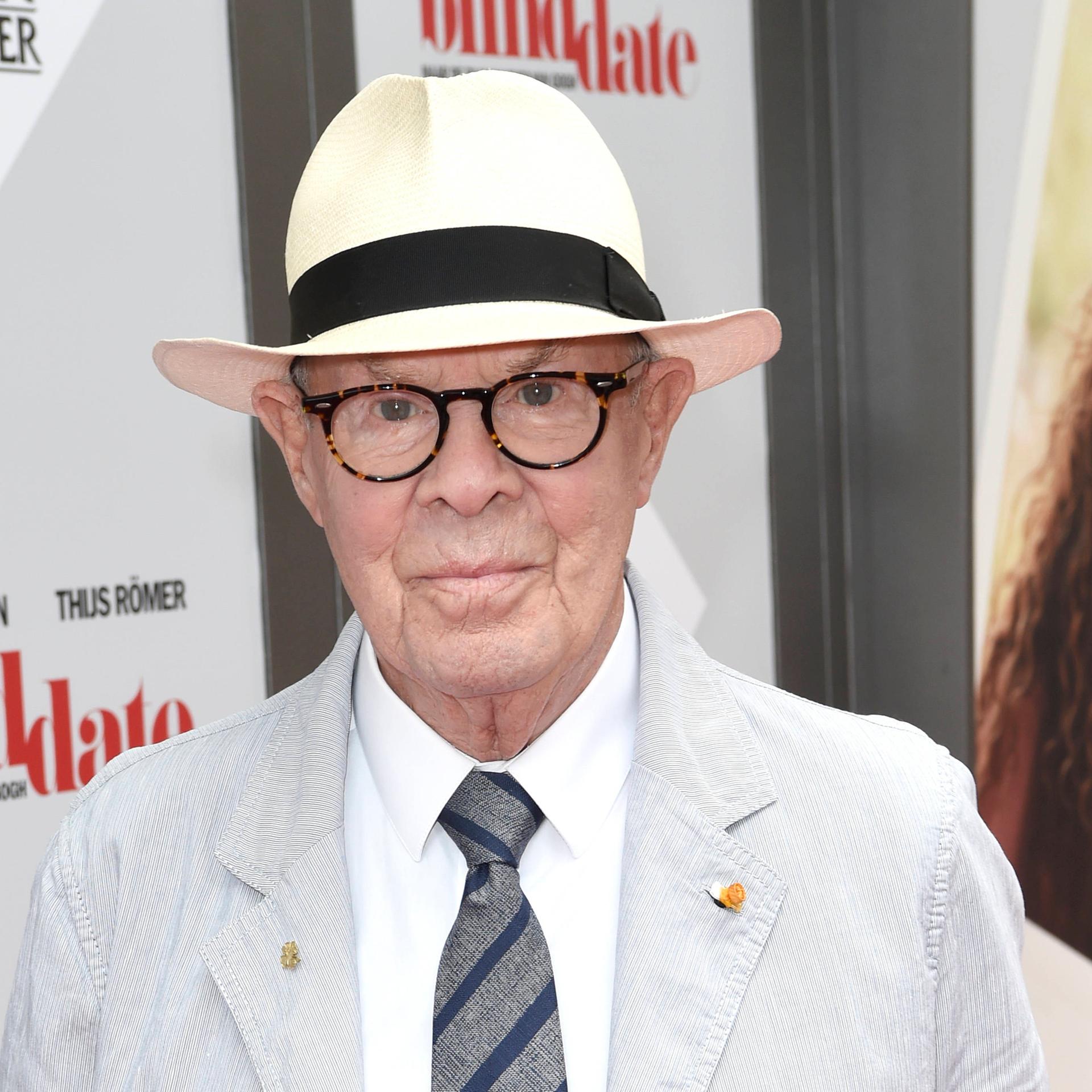 Hans van Manen steht mit weißem Hut vor einem Theatereingang in Amsterdam. 