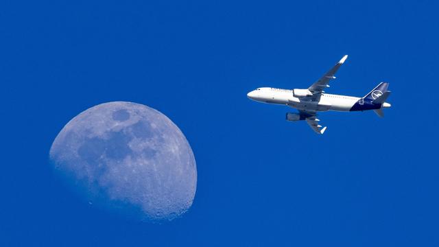 Ein am Flughafen Frankfurt gestartetes Flugzeug der Lufthansa am blauen Himmel vor dem Mond 