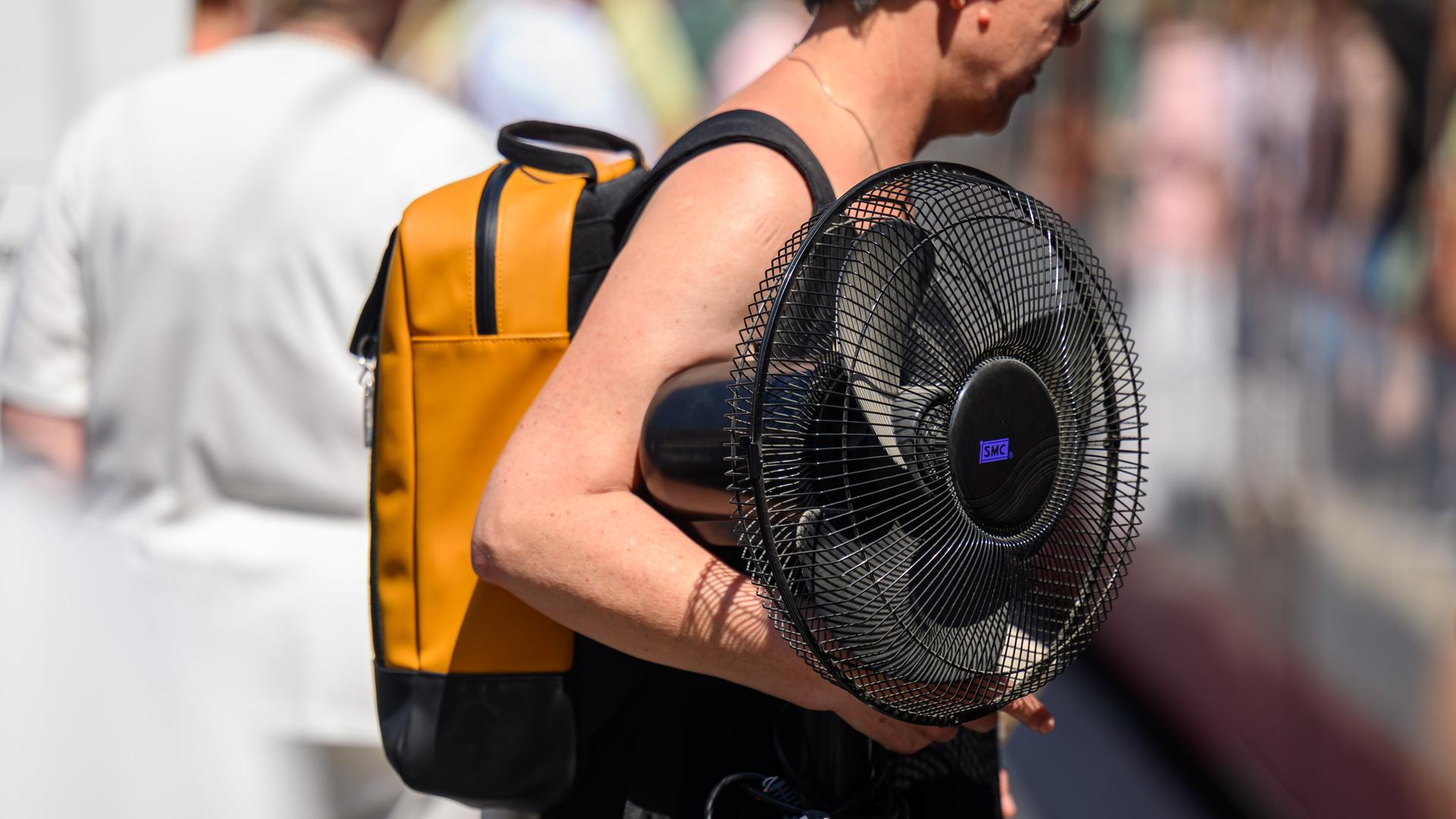 Eine Frau trägt einen Ventilator unter ihrem Arm. 