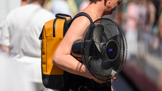 Eine Frau trägt einen Ventilator unter ihrem Arm. 