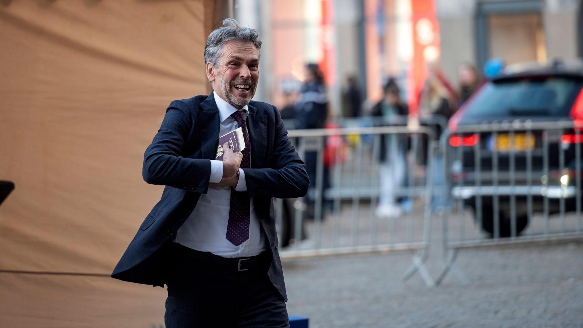 Dick Schoff lacht in die Kamera. Er steckt sich seinen Ausweis in die rechte Jacken-Innentasche. Dick Schoff lacht in die Kamera. Er steckt sich seinen Ausweis in die rechte Jacken-Innentasche.
