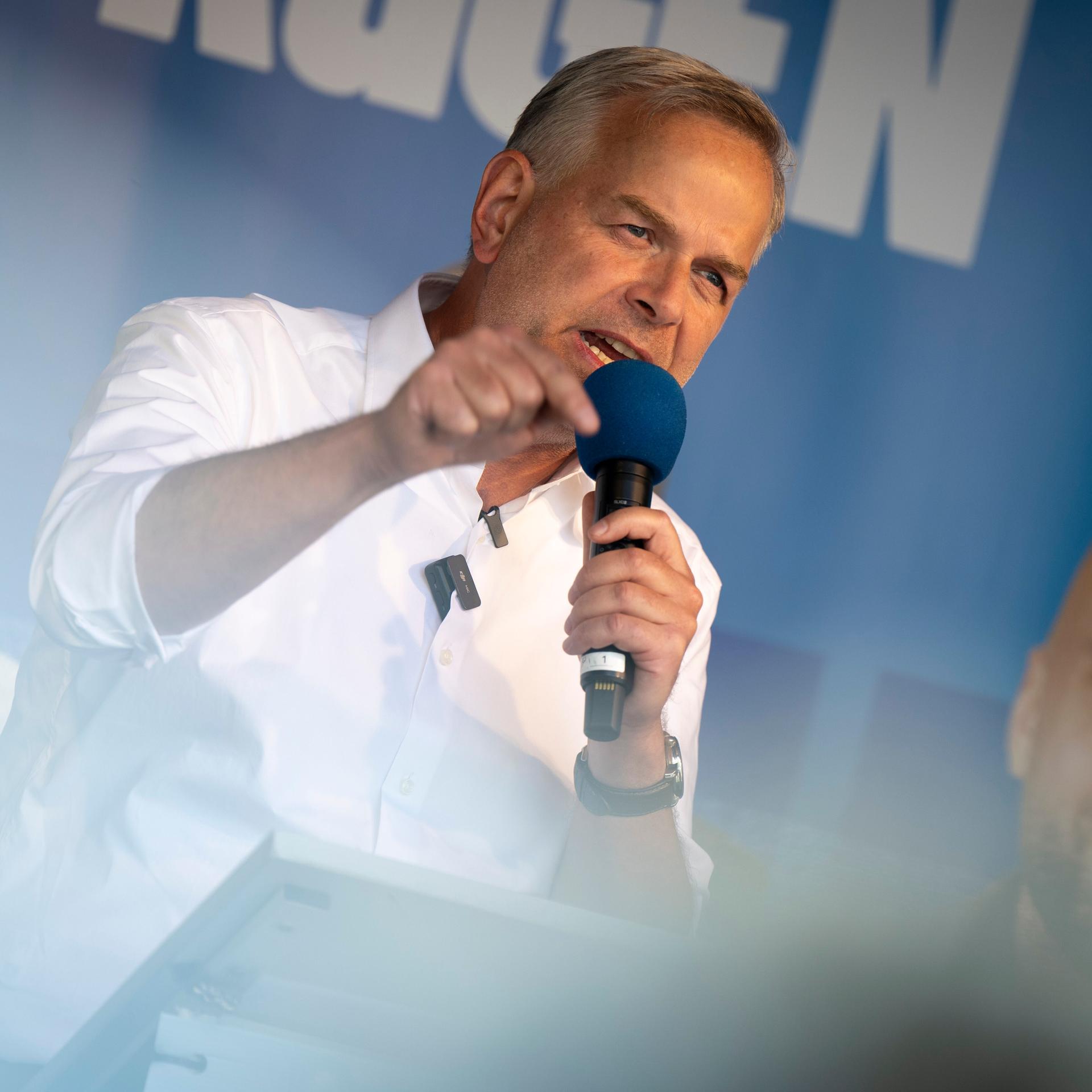 Der AfD-Politiker Leif-Erik Holm steht in Stralsund auf einer Bühne. Er hält ein blaues Mikrofon in der Hand und gestikuliert. Im Hintergrund ist ein blaues Parteibanner zu erkennen.