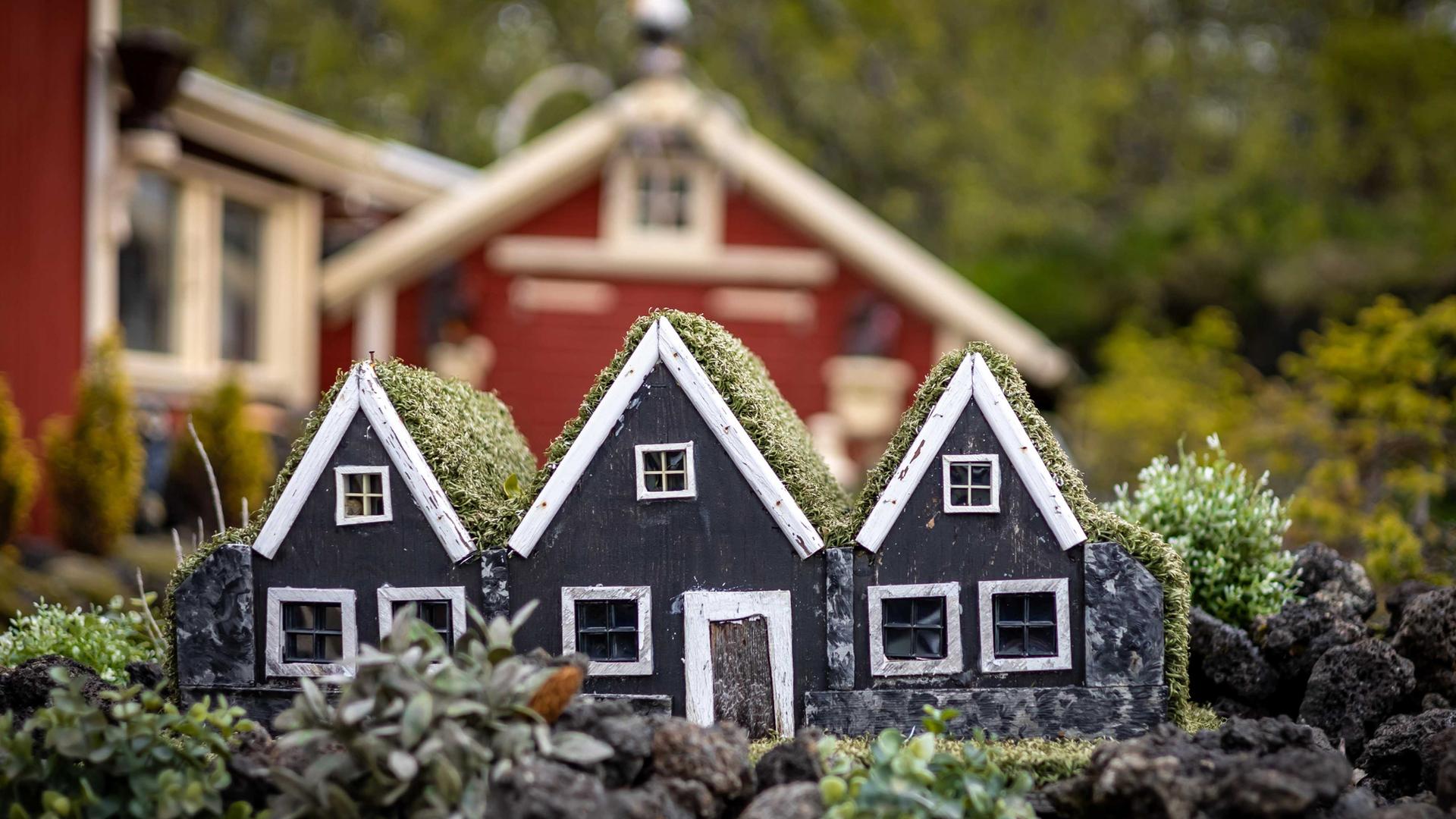 Drei kleine, schwarze Elfenhäuser aus Holz als Gartendekoration vor einem Wohnhaus.