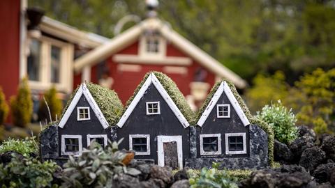 Drei kleine, schwarze Elfenhäuser aus Holz als Gartendekoration vor einem Wohnhaus.