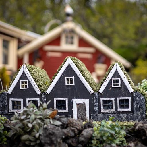 Drei kleine, schwarze Elfenhäuser aus Holz als Gartendekoration vor einem Wohnhaus.