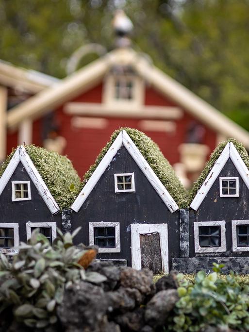 Drei kleine, schwarze Elfenhäuser aus Holz als Gartendekoration vor einem Wohnhaus.
