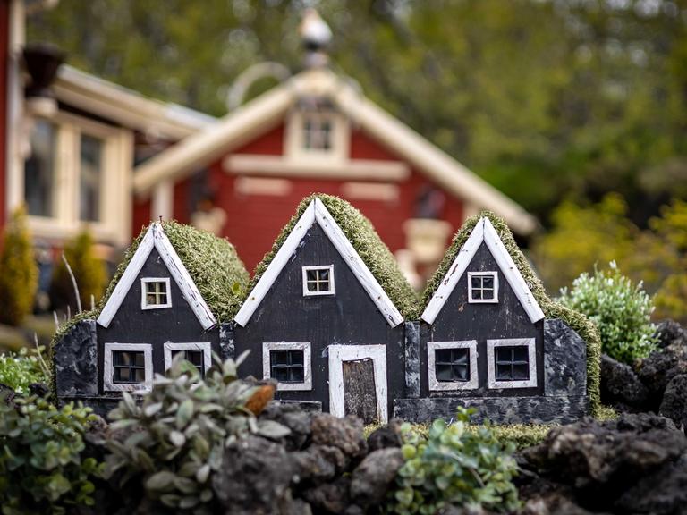 Drei kleine, schwarze Elfenhäuser aus Holz als Gartendekoration vor einem Wohnhaus.