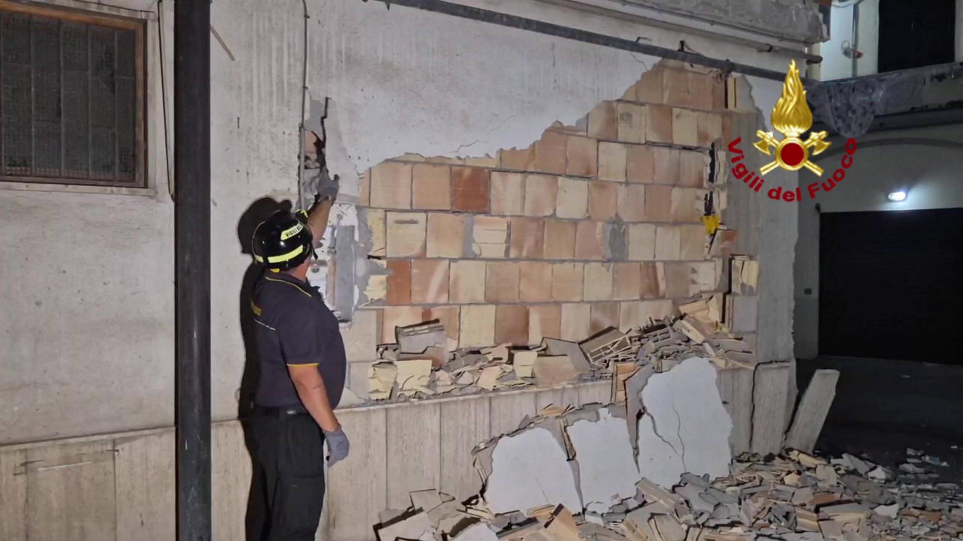 Ein Mann mit Helm steht vor einer beschädigten Häusewand. Ein Mann mit Helm steht vor einer beschädigten Häusewand.