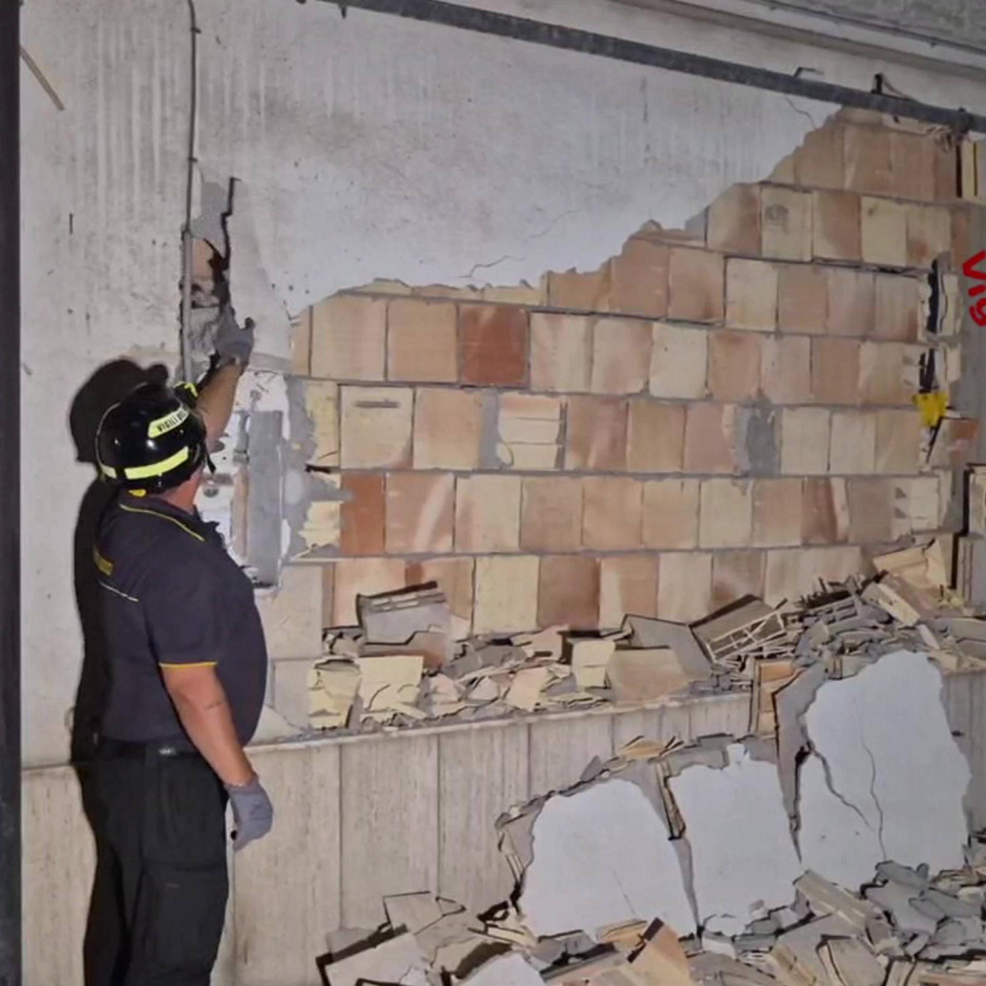Ein Mann mit Helm steht vor einer beschädigten Häusewand.
