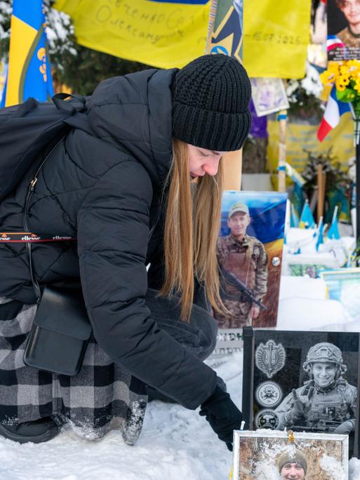 Eine Ukrainierin wischt Schnee von dem Foto ihres an der Front gestorbenen Mannes auf dem Maidan-Platz in Kiew.