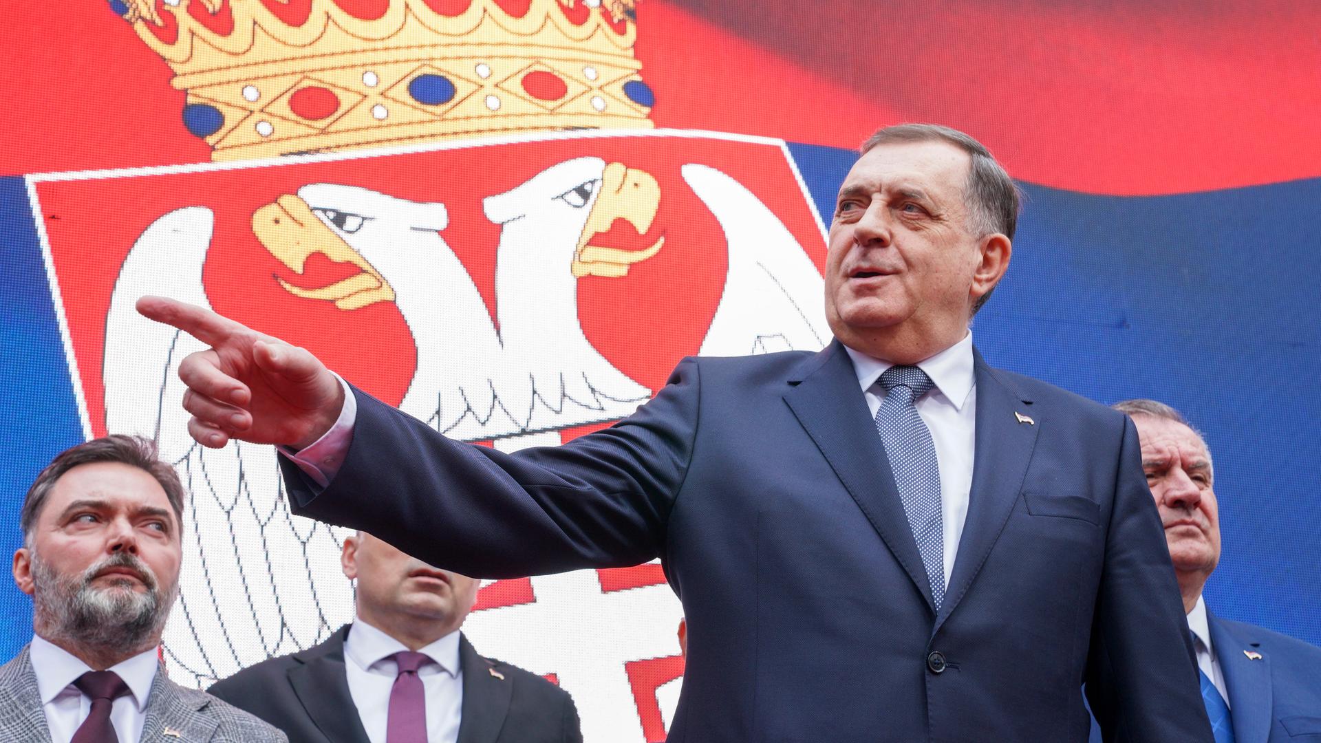 Der bosnisch-serbische Präsident Milorad Dodik steht vor einer Flagge der Republika Srpska in einem schwarzen Sakko.