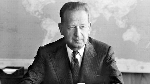Auf dem Foto ist der ehemalige UN-Generalsekretär Dag Hammarskjöld zu sehen. Er trägt einen Anzug und sitzt an einem Schreibtisch. Er kam 1961 Jahren bei einem Flugzeugabsturz ums Leben.