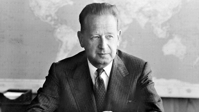 Auf dem Foto ist der ehemalige UN-Generalsekretär Dag Hammarskjöld zu sehen. Er trägt einen Anzug und sitzt an einem Schreibtisch. Er kam 1961 Jahren bei einem Flugzeugabsturz ums Leben.