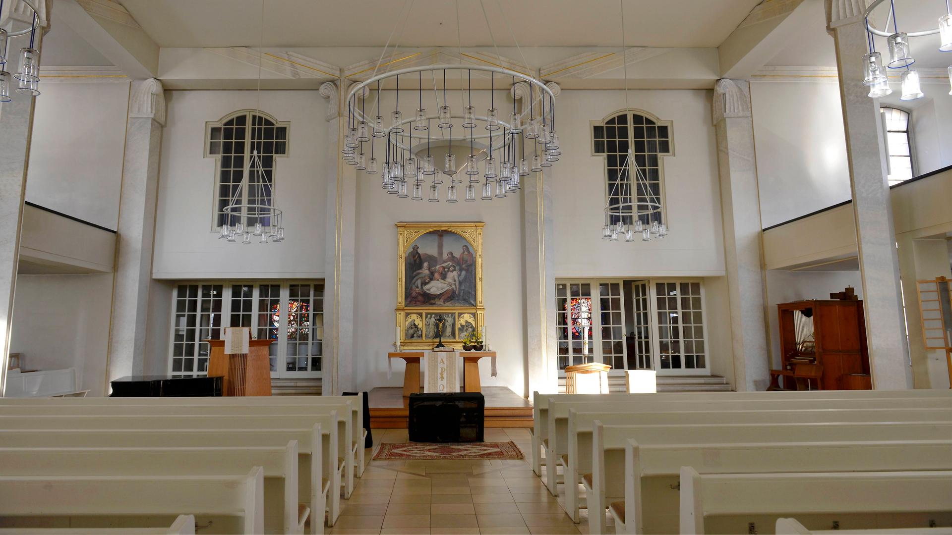 Das Schiff der Luisenkirche in Berlin. Bänke sind angereiht. Alles ist sehr hell. Hinter dem Altar ist ein goldgeschmücktes Bild.