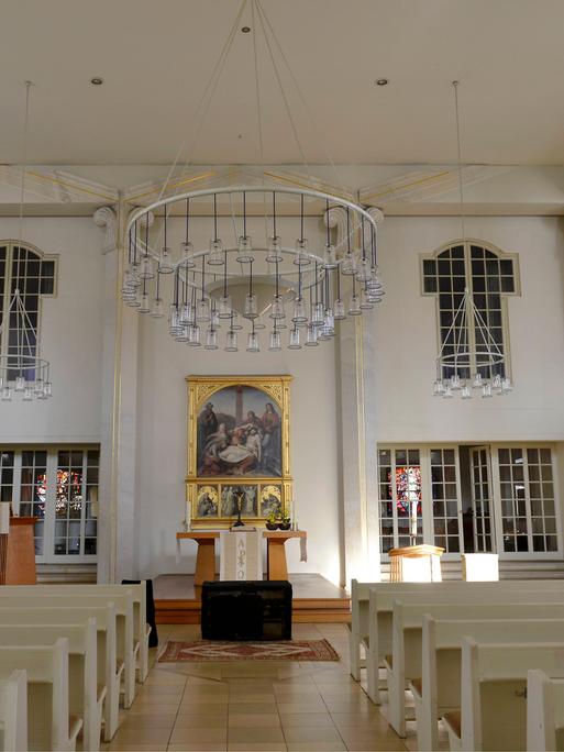 Das Schiff der Luisenkirche in Berlin. Bänke sind angereiht. Alles ist sehr hell. Hinter dem Altar ist ein goldgeschmücktes Bild.