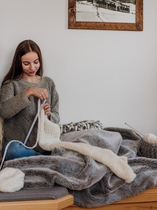 Eine junge Frau sitzt am Kachelofen und strickt.