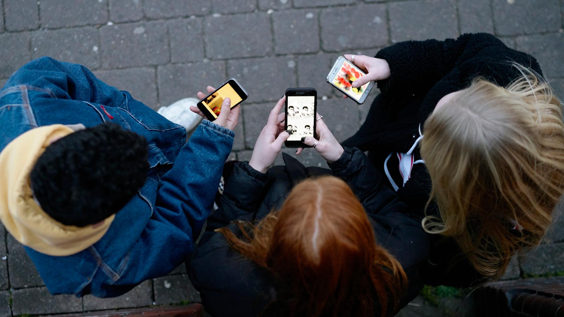Eine Gruppe Jugendlicher von oben fotografiert, sie stehen mit ihren Mobiltelefonen in der Hand nebeneinander. 