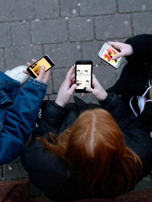 Eine Gruppe Jugendlicher von oben, sie stehen mit ihren Mobiltelefonen in der Hand im Kreis
