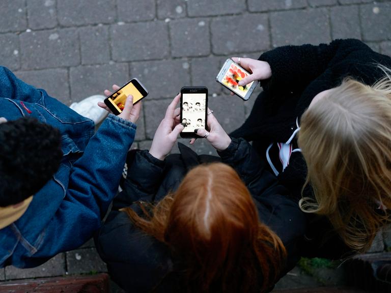 Eine Gruppe Jugendlicher von oben, sie stehen mit ihren Mobiltelefonen in der Hand im Kreis