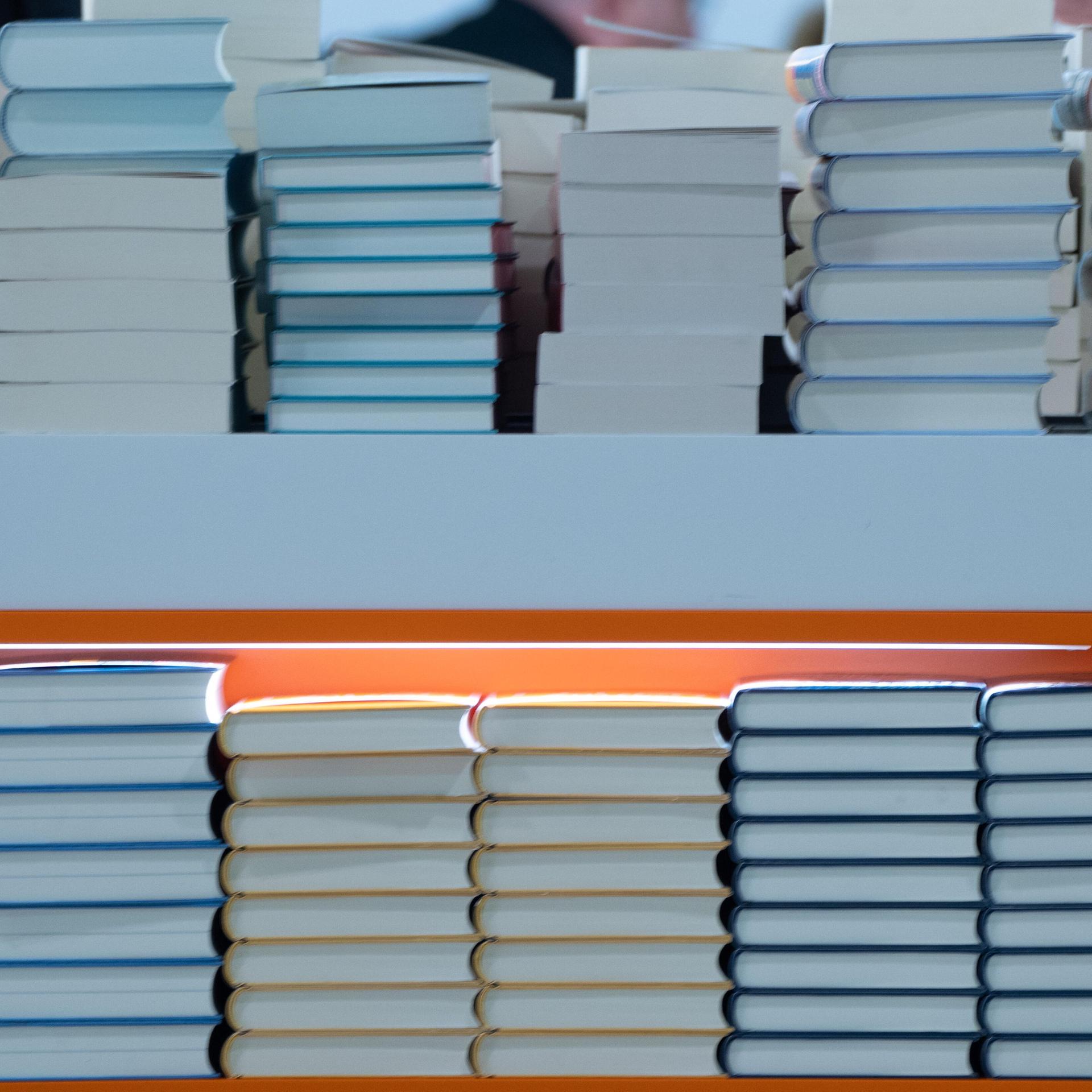In einem Regal liegen Stabel von Büchern. Es ist ein Foto von einer Buchmesse. 
