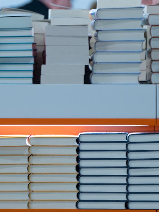 In einem Regal liegen Stabel von Büchern. Es ist ein Foto von einer Buchmesse. 