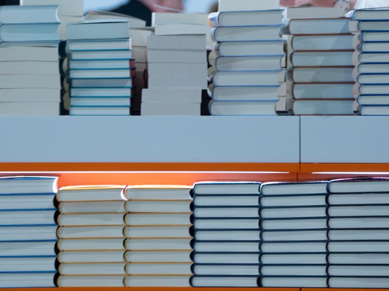 In einem Regal liegen Stabel von Büchern. Es ist ein Foto von einer Buchmesse. 