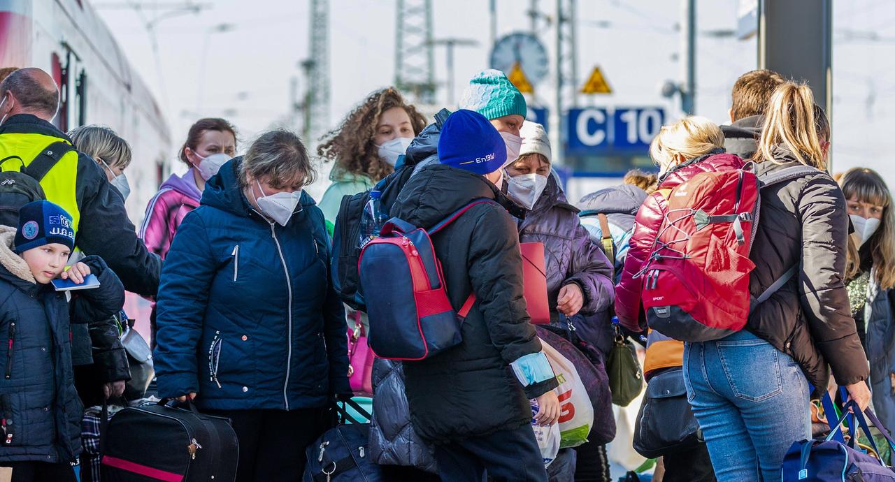 Frauen und KInder mit Masken steigen aus einem Zug und werden von Helfern im Empfang genommen.
