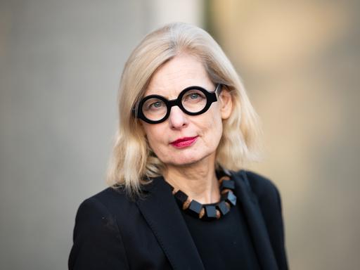 Claudia Guderian trägt eine schwarz umrandete Brille, eine schwarze Kette und ein schwarzes Oberteil. Sie schaut freundlich und direkt in die Kamera.