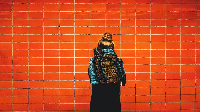 Rückansicht einer Frau, die vor einer rot gekachelten Wand steht