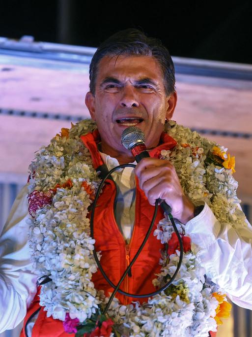 Rodrigo Paz, Boliviens Präsidentschaftskandidat der Christlich-Demokratischen Partei (PDC), hält nach der Stichwahl zur Präsidentschaftswahl eine Rede. Er trägt Blumenschmuck um den Hals und hält den Zeigefinger in die Höhe (La Paz, Bolivien, 19.10.2025)