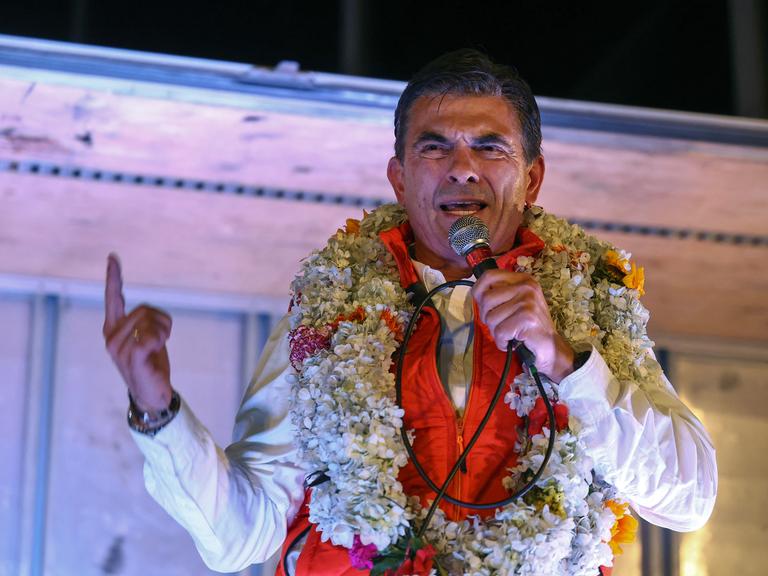 Rodrigo Paz, Boliviens Präsidentschaftskandidat der Christlich-Demokratischen Partei (PDC), hält nach der Stichwahl zur Präsidentschaftswahl eine Rede. Er trägt Blumenschmuck um den Hals und hält den Zeigefinger in die Höhe (La Paz, Bolivien, 19.10.2025)