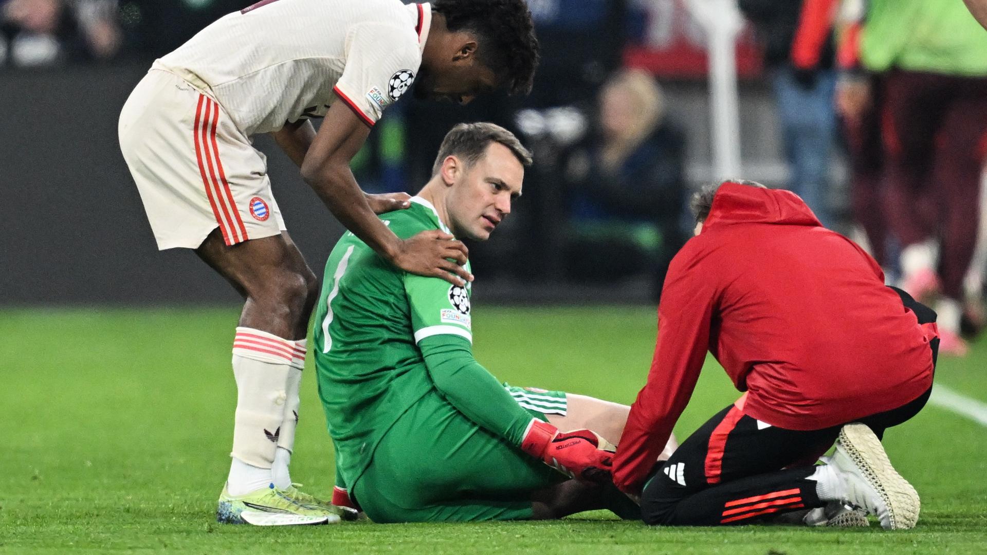 Torhüter Manuel Neuer (M) lliegt auf dem Platz und spricht mit dem Mannschaftsarzt. Hinter ihm ein anderer Bayern-Spieler. Torhüter Manuel Neuer (M) lliegt auf dem Platz und spricht mit dem Mannschaftsarzt. Hinter ihm ein anderer Bayern-Spieler.