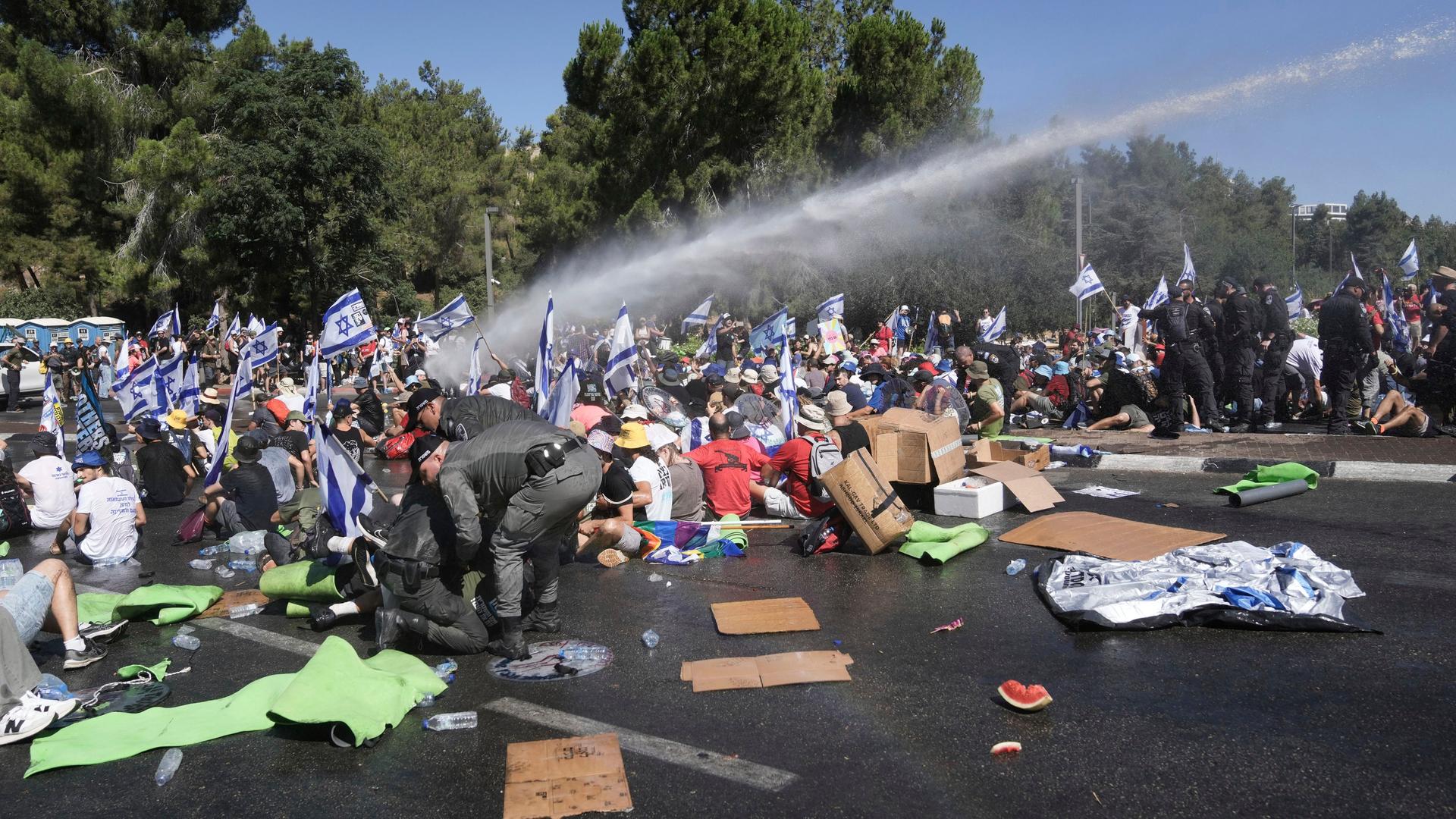 Isralische Polizisten versuchen in Jerusalem, Demonstranten, die auf dem Boden hocken, zu entfernen. Auch Wasserwerfer werden eingesetzt.