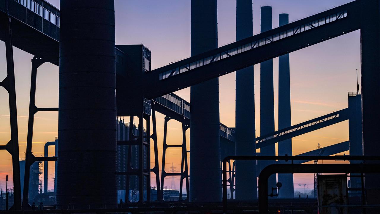 Schornsteine und Bandbrücken der Zeche Zollverein heben sich als Silhouetten vor einem Abendhimmel ab.
