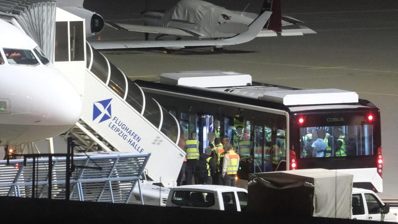 Ein Bus mit Männern begleitet von Bundespolizisten steht auf dem Flughafen Leipzig-Halle an einem Flugzeug. 