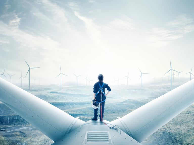 Eine Frau im Blaumann steht auf der Turbine eines Windrades und schaut aufs aufgewühlte Meer.
