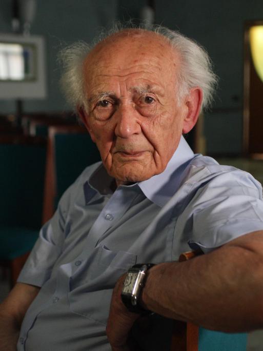 Der britisch-polnische Soziologe Zygmunt Bauman sitzt auf einem Stuhl und schaut seitlich gedreht direkt in die Kamera. 