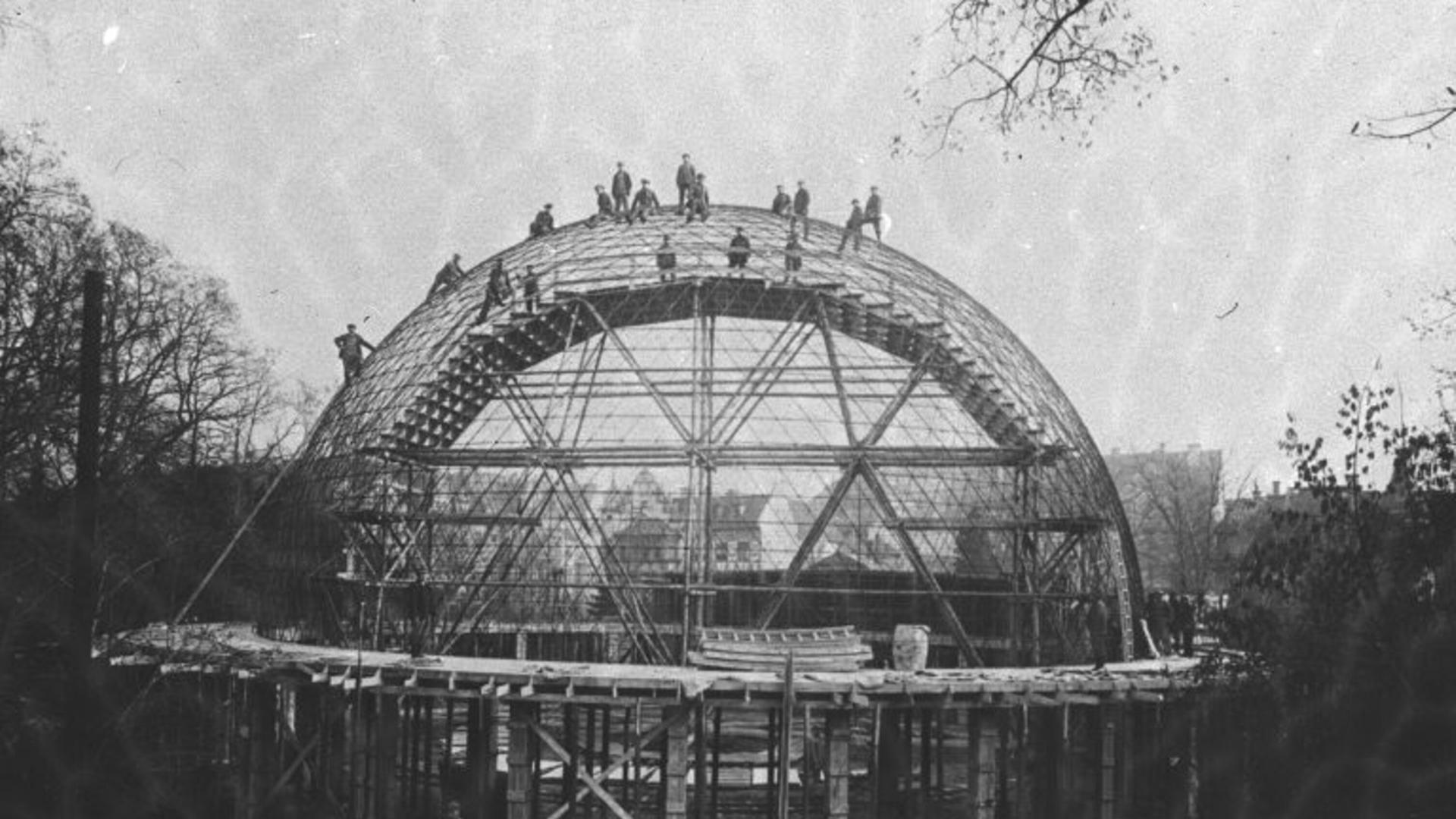 Schwarz-Weiß-Illustation: Auf der Kuppel des Planetariums stehen Menschen, vermutlich jene, die die Kuppel erbauen. Im Vordergrund Baumaterialen wie Hölzer.