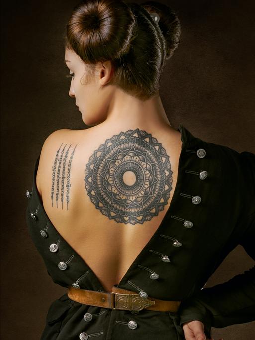 Frau zeigt ihr Mandala-Tattoo auf dem Rücken.