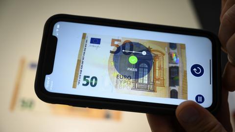 Ein Mitarbeiter prüft die Echtheit einer Euro-Banknote mit seinem Smartphone.