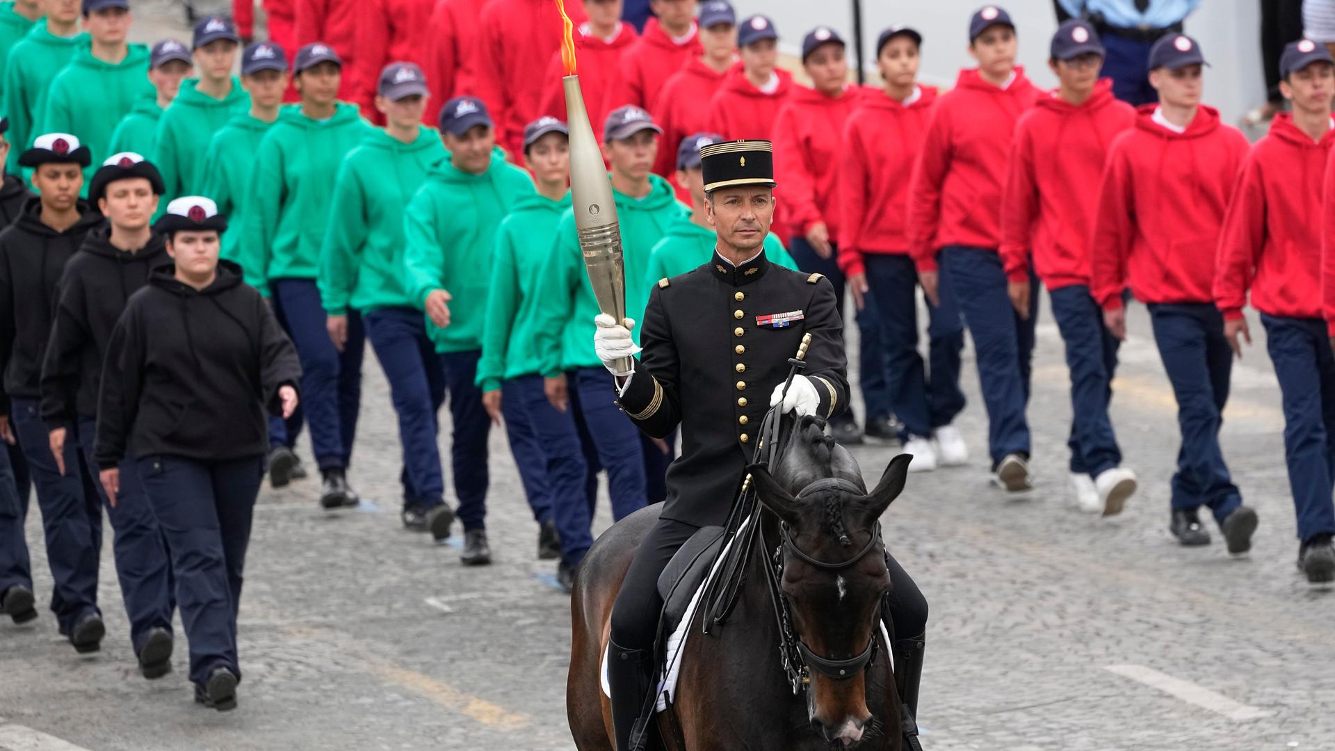 Nationalfeiertag in Frankreich: Der Chef der französischen Elite-Reitschule Cadre Noir, Thibaut Vallette, sitzt auf einem Pferd und trägt die Olympische Flamme. 