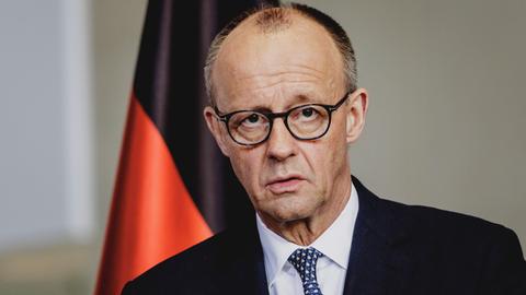 Das Bild zeigt Friedrich Merz mit ernster Mine vor einer Deutschland-Flagge.