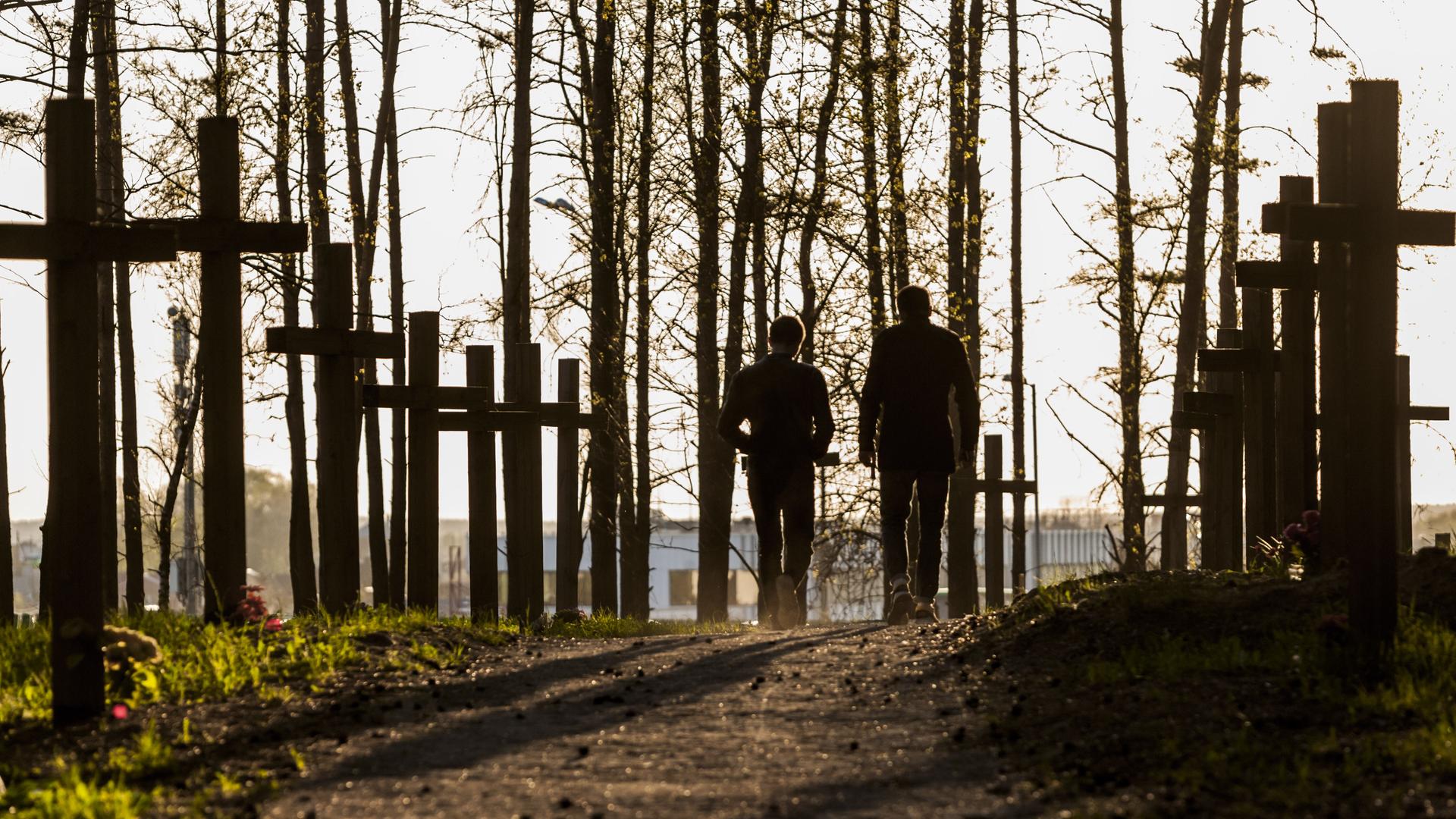 Zwei Personen spazieren über einen Waldweg, der von Gedenkkreuzen gesäumt ist.