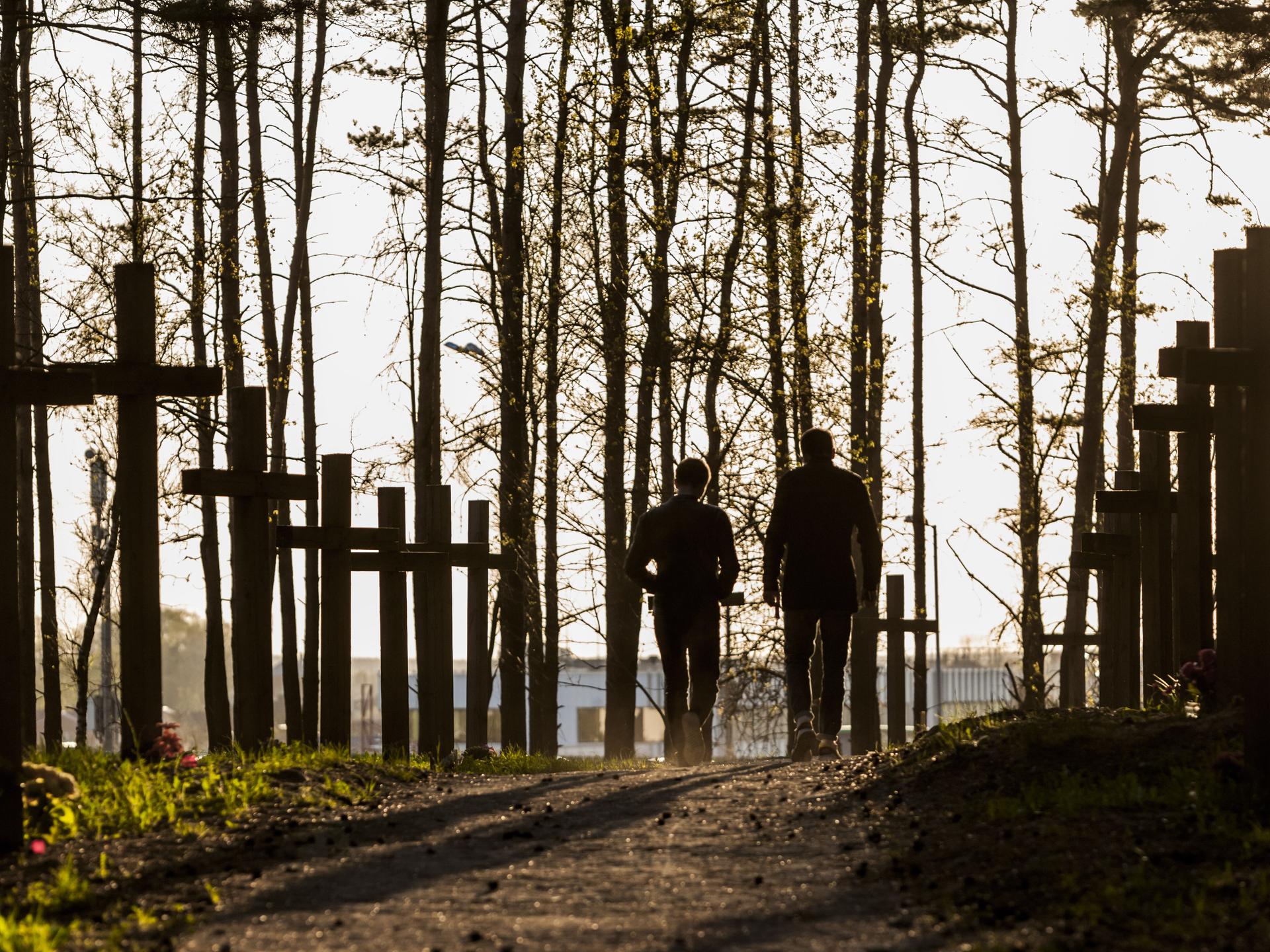 Zwei Personen spazieren über einen Waldweg, der von Gedenkkreuzen gesäumt ist.