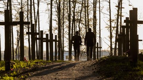 Zwei Personen spazieren über einen Waldweg, der von Gedenkkreuzen gesäumt ist. Zwei Personen spazieren über einen Waldweg, der von Gedenkkreuzen gesäumt ist.
