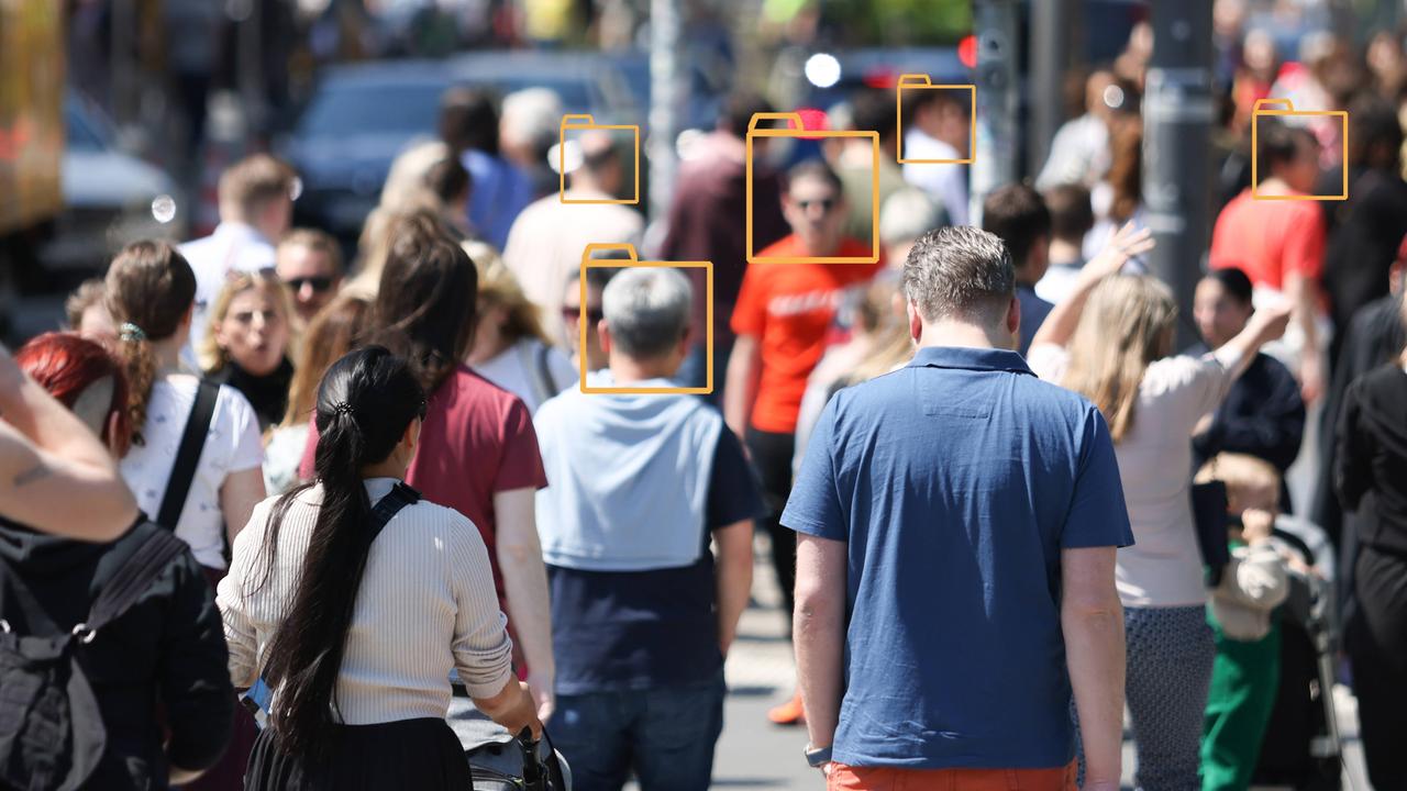 Unscharfes Bild einer Menschenmenge in einer Fußgängerzone. Über manche Gesichter wurden grafische Symbole von Aktenordnern gelegt.