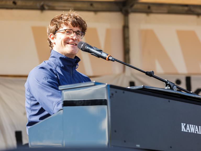 Bodo Wartke sitzt auf einer Bühne am Keyboard und singt