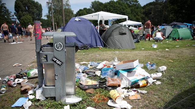 Die Müll-Tonne ist voll. Müll liegt überall auf dem Boden. Dahinter sieht man Zelte. 