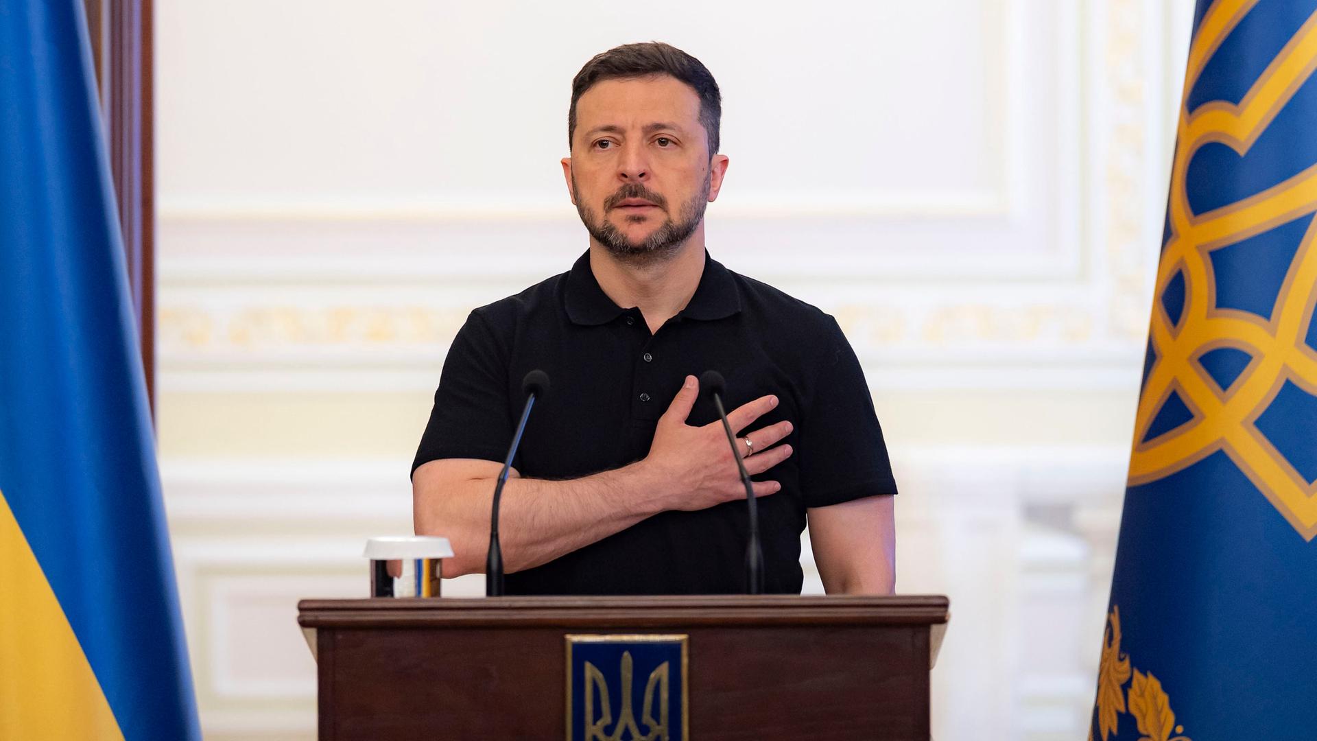 Der ukrainische Päsident Wolodymyr Selenskyj steht hinter einem Rednerpult und legt dabei die rechte Hand auf seinen Brustkorb.