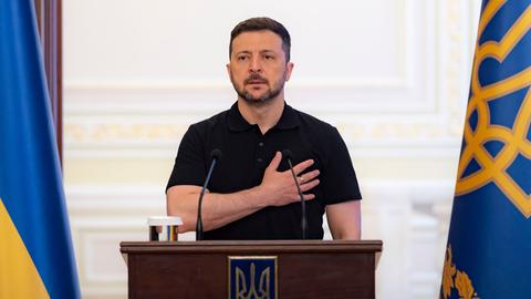 Der ukrainische Päsident Wolodymyr Selenskyj steht hinter einem Rednerpult und legt dabei die rechte Hand auf seinen Brustkorb.